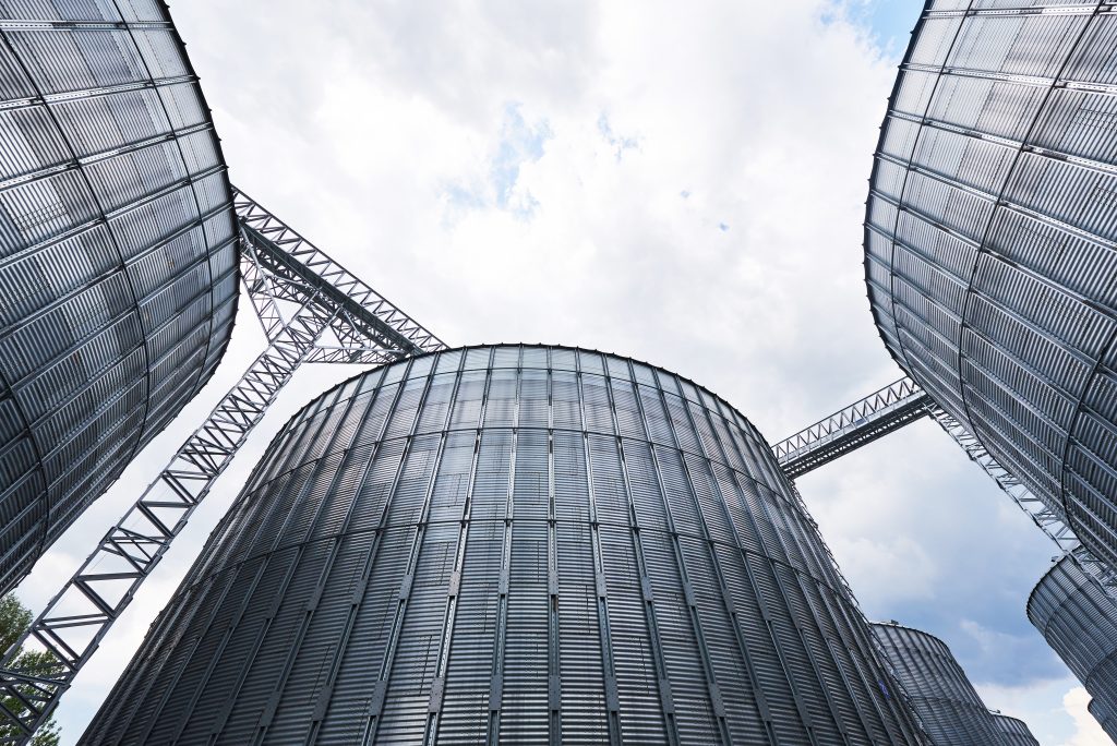 Agricultural Silos. Building Exterior. Storage and drying of grains, wheat, corn, soy, sunflower against the blue sky with white clouds.
