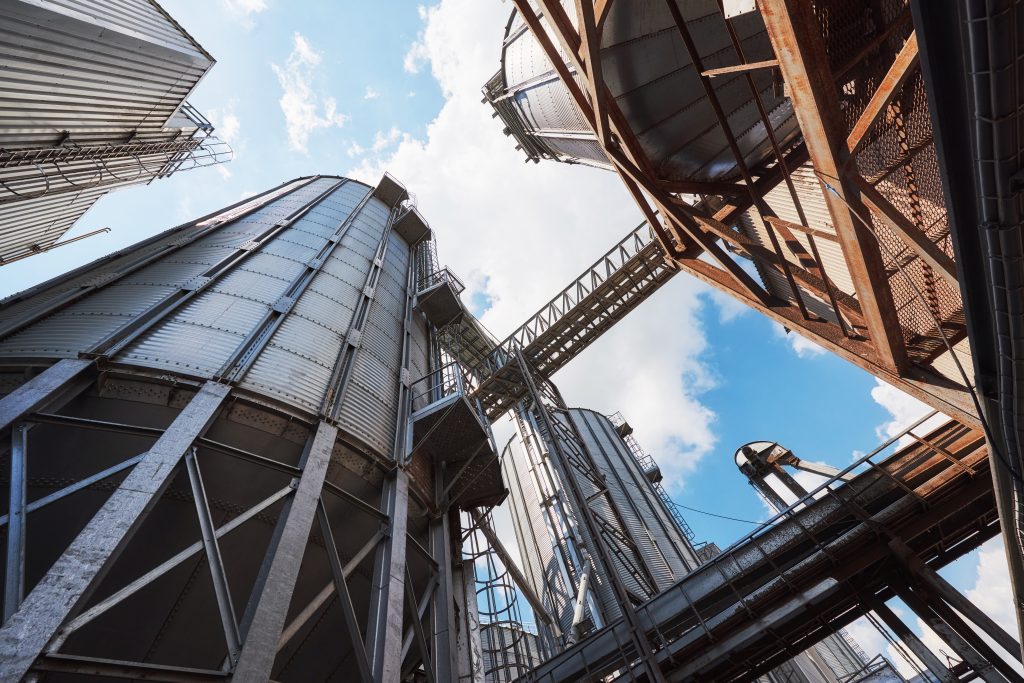 Agricultural Silos. Building Exterior. Storage and drying of grains, wheat, corn, soy, sunflower against the blue sky with white clouds.